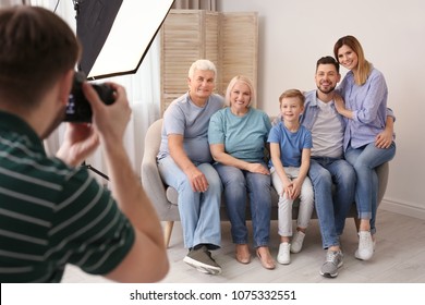 Professional Photographer Taking Photo Of Family On Sofa In Studio