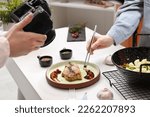 Professional photographer taking photo while food stylist decorating composition with meat medallion in studio, closeup