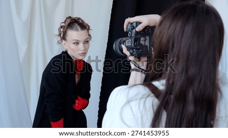 Professional photographer using digital camera while shooting fashion model, creating elegant studio portrait with dramatic lighting and dynamic pose