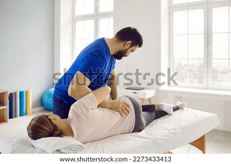 Professional physiotherapist, chiropractor, osteopath, or manual therapist helping young woman, treating her back pain, making her muscles relax. Physical therapy, rehabilitation, pain relief concept