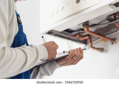 Professional Plumber Checking A Boiler At Home And Writing On A Clipboard