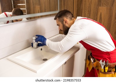 Professional plumber, male worker in uniform installing sink and water pipe in new apartment