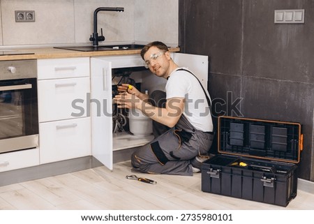 Professional plumber working on installing or repairing water filter system under sink in modern kitchen