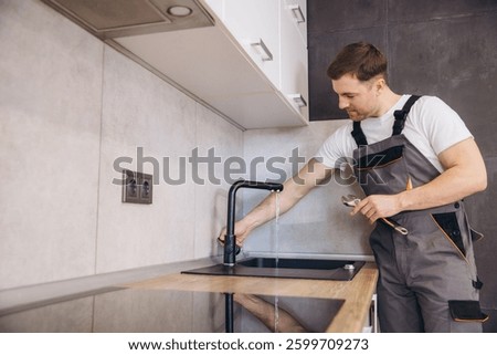 Professional plumber working on kitchen faucet, using wrench and checking water flow in modern apartment