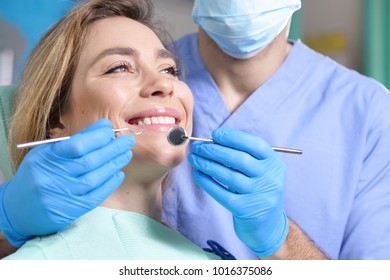 In a professional practice, a dentist checks the dentition of the patient, and she is happy with the visit, smiling, showing the perfect white teeth. Concept of: dentists, healthcare, perfect smile. - Shutterstock ID 1016375086