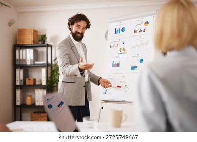 A professional is presenting data charts and graphs during a business meeting at an office. Team members are engaged and listening carefully to the presentation.