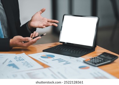 Professional presenting financial data using a digital tablet, surrounded by charts and a calculator on a wooden desk.
