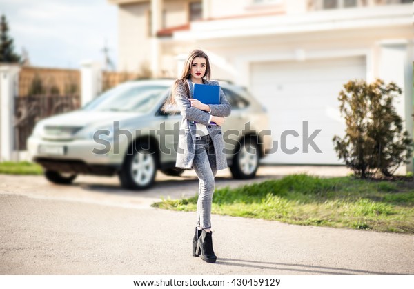 Professional property saleswoman, gesture and\
people concept - happy businesswoman with folder giving key over\
property and car\
background