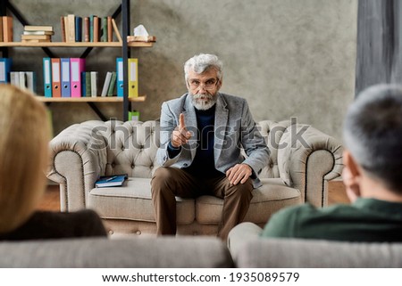 Professional psychoanalyst talking to upset couple of spouses sitting on sofa during session in cabinet, selective focus. Psychotherapy concept