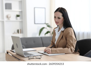Professional psychologist taking notes while working with laptop at table in office