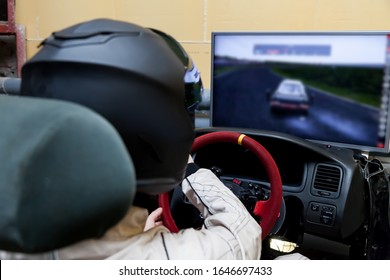 A professional racer in a black helmet and a white homologated suit sits in the sports seat of a car for drifting and racing during a race and training on a simulator.
