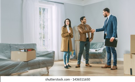 Professional Real Estate Agent Shows Bright New Apartment to Young Couple. Successful Young Couple Becoming Homeowners, Seal the Deal with Real Estate Broker by Handshake. Bright Home with Big Windows - Powered by Shutterstock