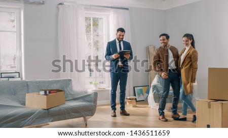 Professional Real Estate Agent Shows Bright New Apartment to a Young Couple. Successful Young Couple Ready to Become Homeowners. Spacious Bright Home with Big Windows.