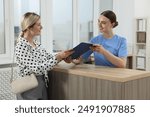 Professional receptionist working with patient at wooden desk in hospital