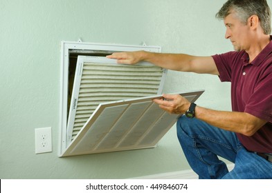 Professional repair service man or diy home owner removing a dirty air filter on a house air conditioner so he can replace it with a new clean one.