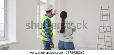 Professional repairman explaining future home design plan to young woman. View from behind of builder and homeowner talking about house design, interior decoration while meeting at home