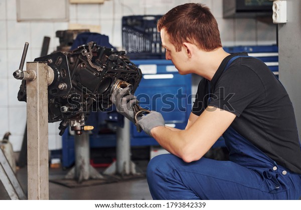 Professional repairman in garage works with\
broken automobile\
engine.