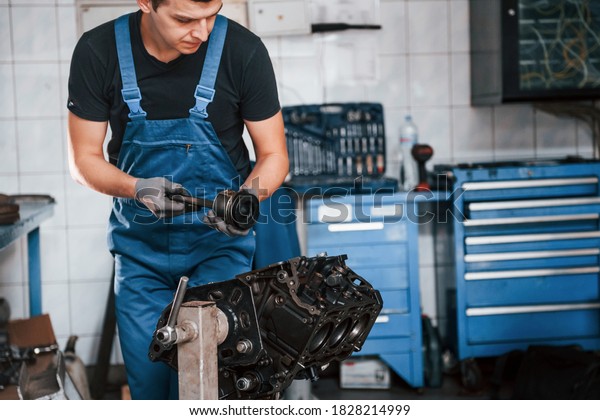 Professional repairman in garage works with\
broken automobile\
engine.