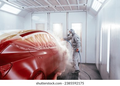 Professional repairman painting car in a spray booth at a professional car service.