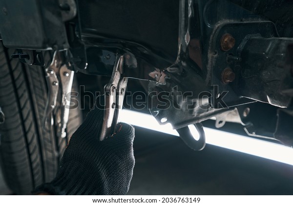 Professional repairman placing locking pliers under\
the car