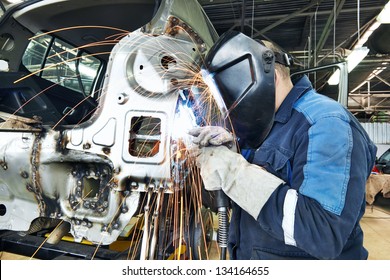 professional repairman worker in automotive industry welding metal body car with sparks - Powered by Shutterstock