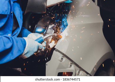 professional repairman worker in automotive industry welding metal body car with sparks.