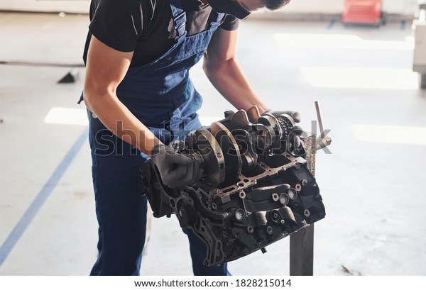 Professional repairman works with broken\
automobile engine.
