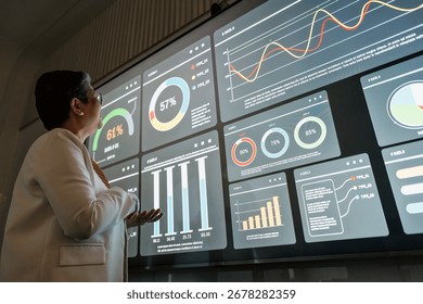 Professional reviews interactive data dashboard with charts and graphs on a large digital screen in a modern office, illustrating analytics, performance tracking, and decisions.