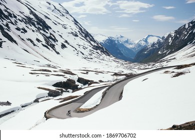 Professional road cyclist on winding mountain pass road in winter. Cycling on road covered in snow. Beginning or end of season. Road cycling in winter