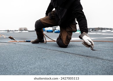 professional roofer applying bitumen roll on flat roof with a gas burner at a modern construction site