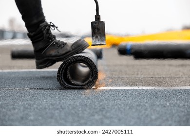 professional roofer at work securing rolled tar paper with a blowtorch on a flat roof installation process