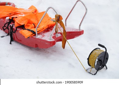 Professional Safety Red Sledge With Orange Life Jackets And Rope On Coil On White Snow Background At Frozen Winter Day - Outdoor Rescue Equipment On Water Ice Hole 