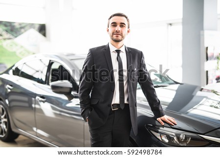 Professional salesman smiling in front of a new car at the dealership profession occupation job owning buy retail luxury lifestyle concept