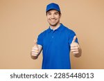 Professional satisfied delivery guy employee man wear blue cap t-shirt uniform workwear work as dealer courier showing thumb up like gesture isolated on plain light beige background. Service concept