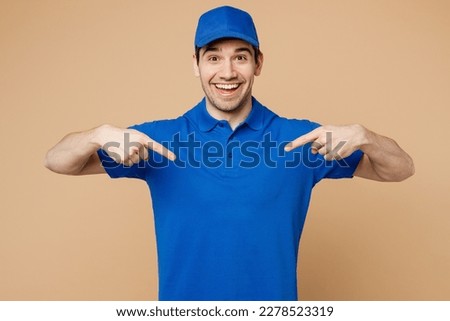 Professional satisfied delivery guy employee man wear blue cap t-shirt uniform workwear work as dealer courier point index fingers on himself isolated on plain light beige background. Service concept