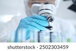 Professional scientist in protective gear is using microscope in a laboratory setting, close-up. Science and medicine concepts