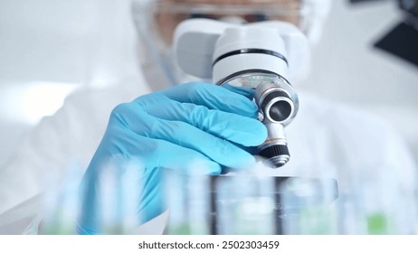 Professional scientist in protective gear is using microscope in a laboratory setting, close-up. Science and medicine concepts - Powered by Shutterstock