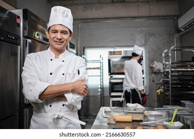 Professional senior Asian male chef in white cooking uniform, food occupation looks at camera, arms crossed, cheerful smile, expertise in commercial pastry culinary jobs, catering restaurant kitchen. - Powered by Shutterstock