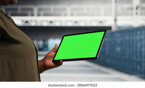 IT professional in server facility working with green screen digital tablet to ensure error free supercomputers networks.