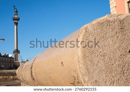 A professional shot featuring a large segment of the original granite shaft from Sigismund's Column, lying near its modern replacement in Warsaw's Castle Square. The focus on the stone's texture tells a story of survival and reconstruction.