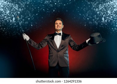 Professional showman wearing suit standing isolated on black and red background holding top hat and pimp cane starting show smiling confident