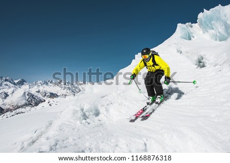 Professional skier at the speed before jumping from the glacier in winter against the blue sky and mountains