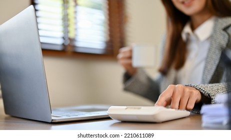 Professional And Smart Asian Female CEO Or Accountant Using Calculator To Calculate And Check Her Financial Data On The Report At Her Desk. Cropped And Close-up Image