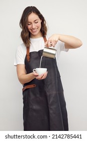 Professional Smiling Barista Woman In Studio Serving Coffee, Pour Milk From A Jug In A Coffee Cup. Café Latte. Isolated On White Background.