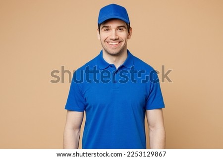 Professional smiling fun satisfied happy delivery guy employee man wear blue cap t-shirt uniform workwear work as dealer courier look camera isolated on plain light beige background. Service concept