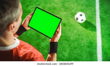 Professional Soccer Player Holding Digital Tablet Computer with Green Screen Chroma Key Template. Elevated Top Down Above Shot of Football Star Browsing Content While Standing on Game Field - Powered by Shutterstock