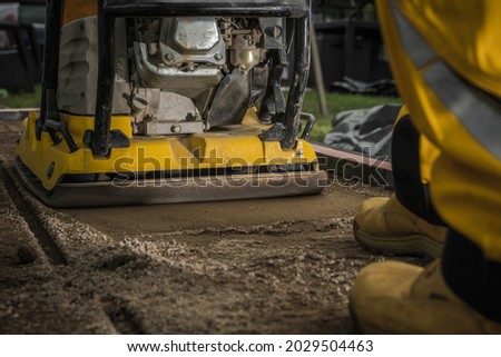 Professional Soil Compactor Job Close Up. Building Concrete Tiles Garden and Patio Pathway. Powerful Machine Compacting Sand.