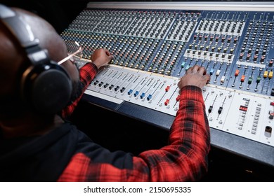 Professional sound engineer producing recording in studio adjusting sound settings at mixing console