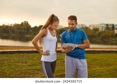 Professional sports coach offers individual training program to young female athlete. Beautiful slim woman in tank top looks at clipboard with fitness workout plan that male personal trainer shows her - Powered by Shutterstock