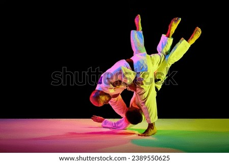 Professional sportsmen, athletic men in white uniform performing technical skills while fighting in mixed neon light isolated black background. Concept of martial art, combat sport, energy.